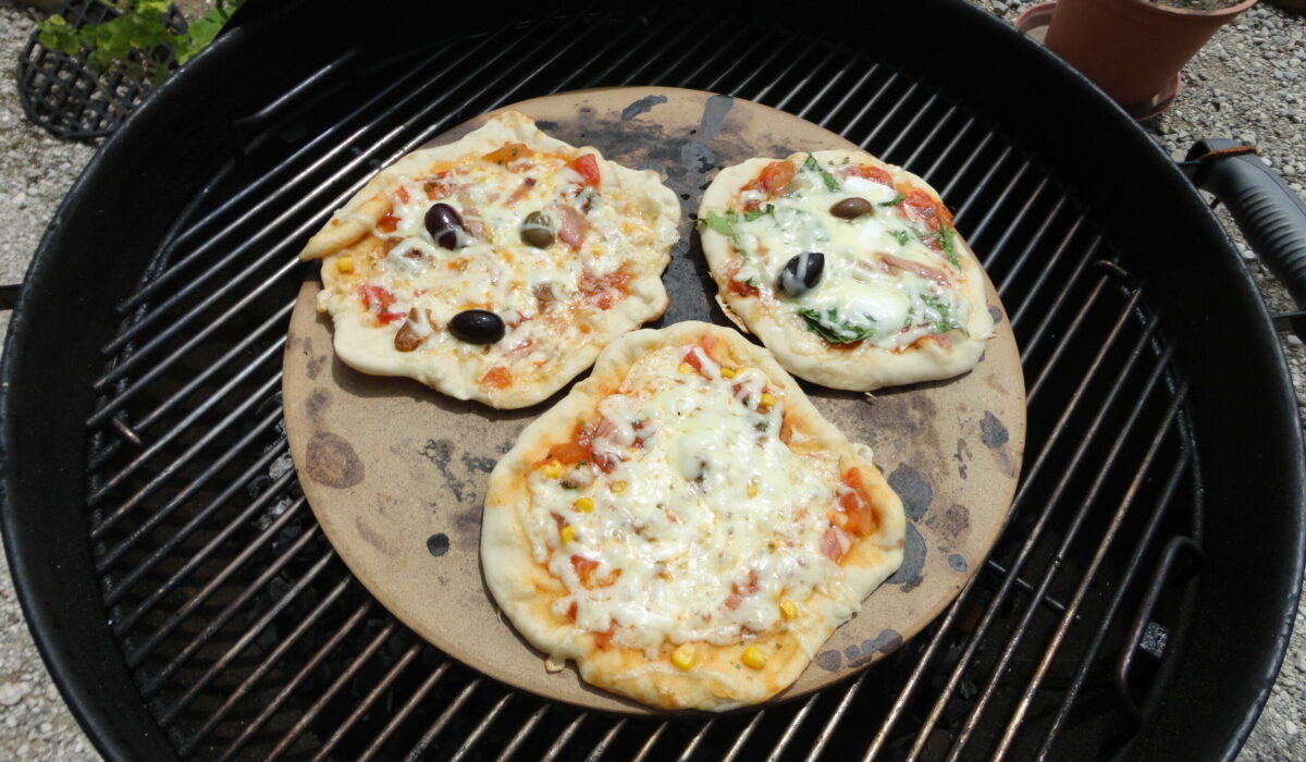 Drei kleine Pizzen auf einem Pizzastein auf einem Griller.