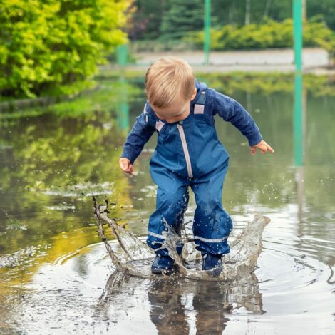 Kind mit Regenhose spielt in einer Pfütze.