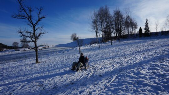 Mutter und Tochter beim Rodeln auf einer verschneiten Wiese.