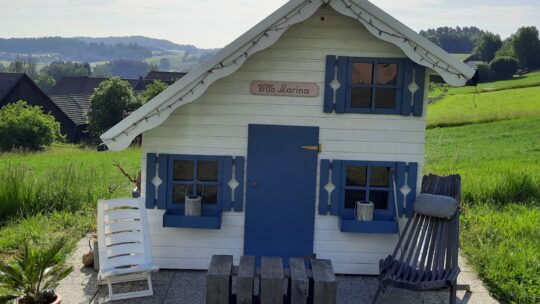 Wweiß-blaues Holzspielhaus auf grüner Wiese